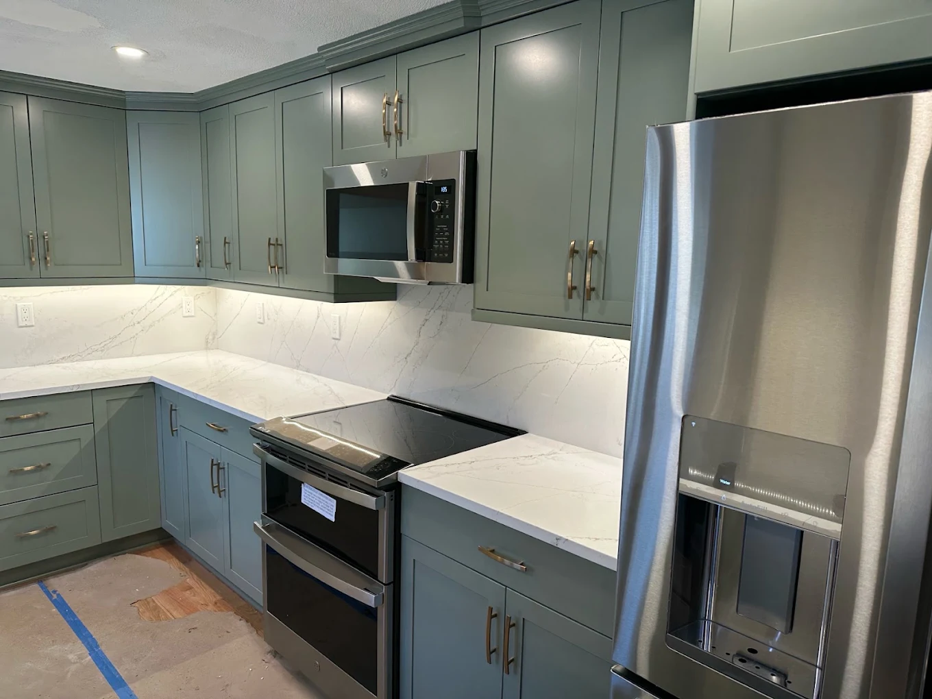 Under-cabinet LED lighting washing a marble backsplash in a kitchen with green cabinets